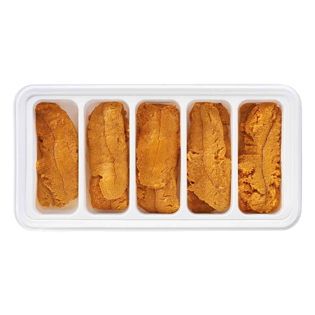 Obenansicht einer weißen Schale mit fünf Portionen orangefarbenem Seeigelrogen (Uni) in einzelnen Fächern, bereit für Sushi oder Sashimi