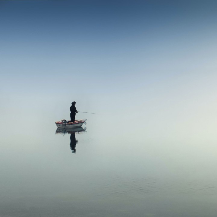 Person angelt allein auf kleinem Boot im Nebel